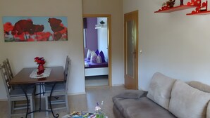 Een woonkamer met een eettafel, een bank en een bed op de achtergrond.