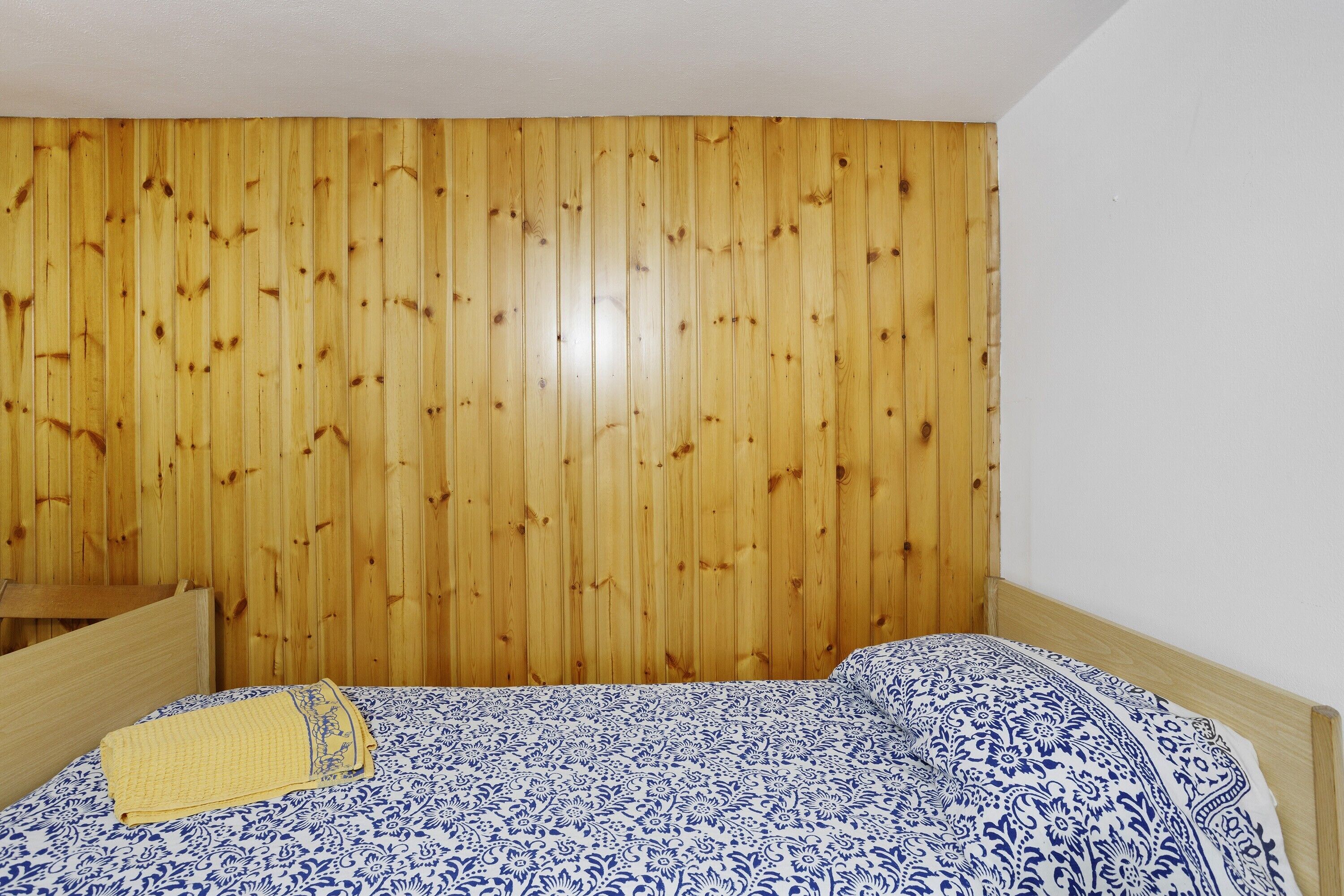 A bedroom with a wooden headboard, a bed with a patterned bedspread, and a small wooden nightstand.
