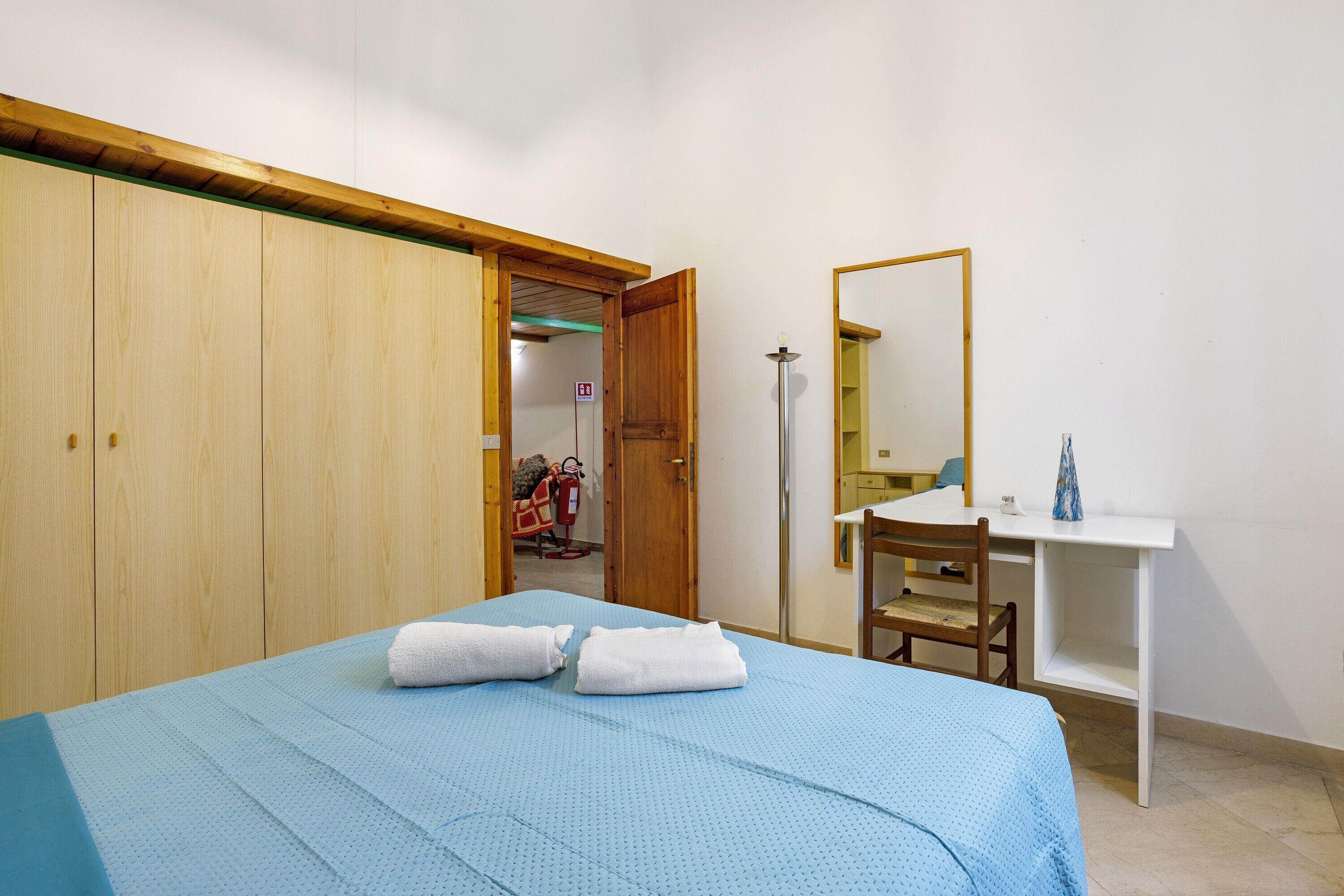 Une chambre à coucher comprenant un lit, un bureau, une chaise, une armoire et un miroir.