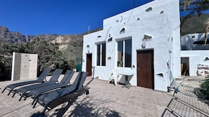 A white building with a pool, lounge chairs, and a mountain view.