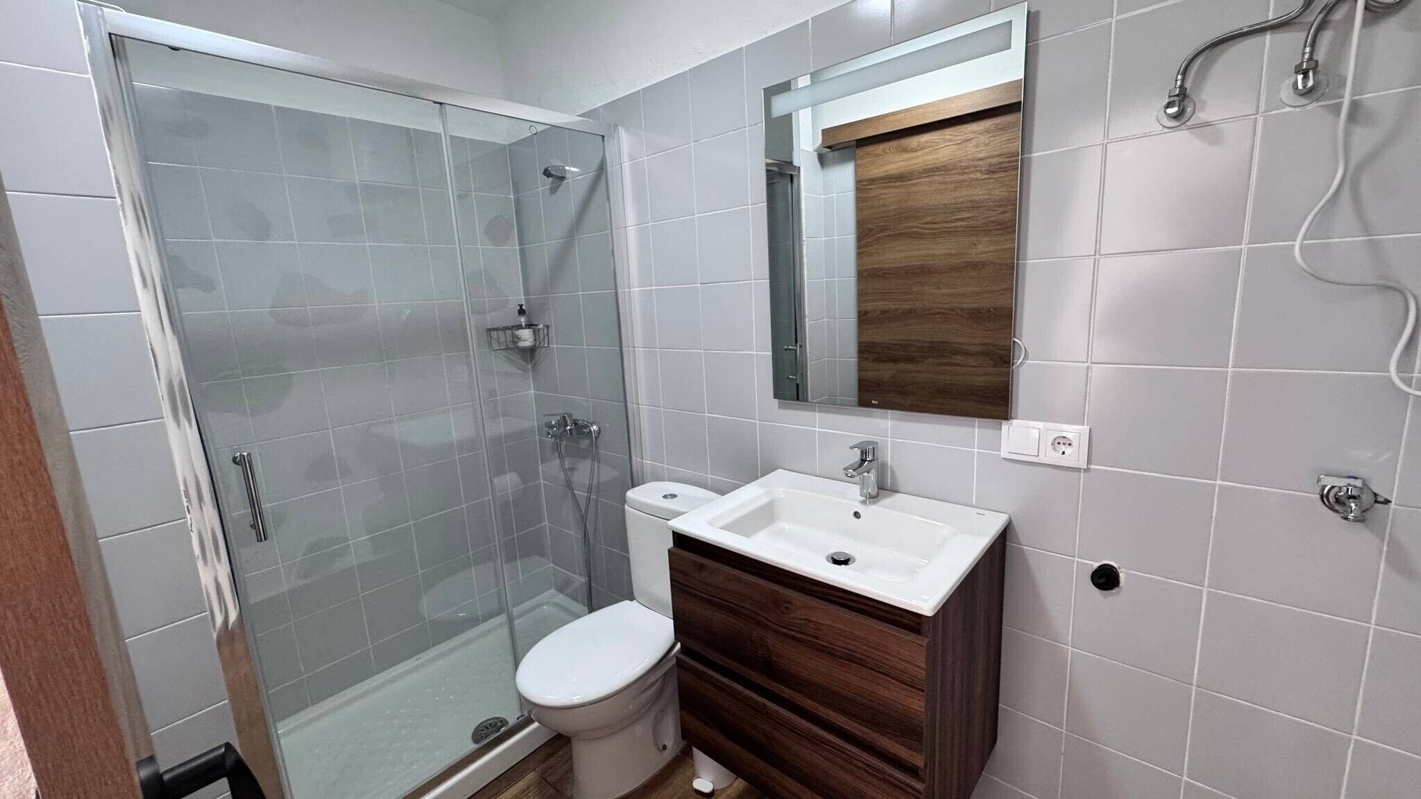 Ein Badezimmer mit Duschkabine aus Glas, einer weißen Toilette, einem Waschbecken mit Holzschrank und einem Spiegel über dem Waschbecken.
