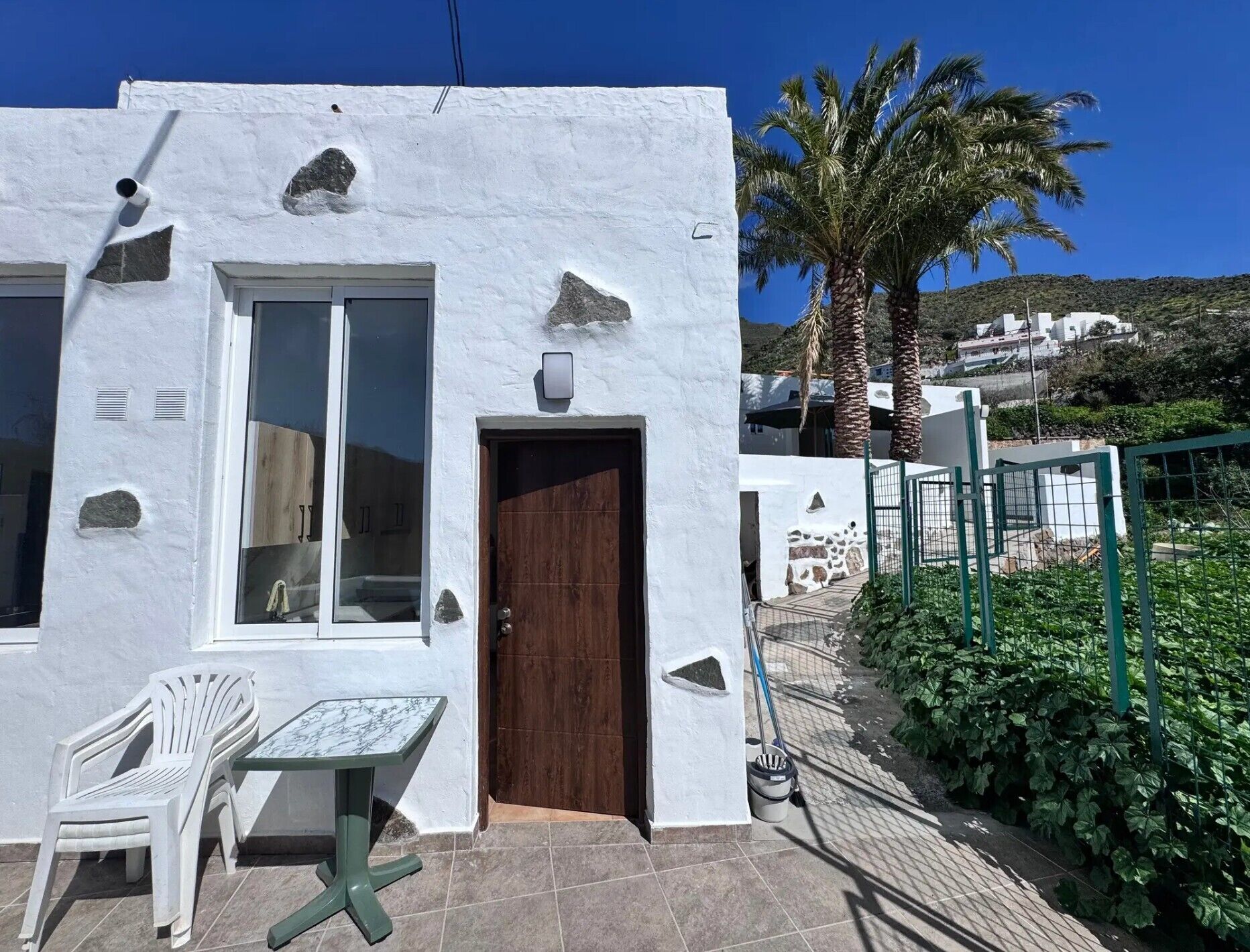 Un bâtiment blanc avec une porte en bois, une fenêtre et une table avec des chaises à l’extérieur.