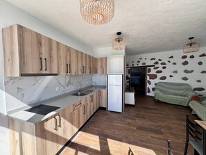 A modern kitchen with wooden cabinets, a built-in sink, and a refrigerator. There is a dining area with a table and chairs. The room has a stone wall and a ceiling with woven light fixtures. - 'Casa 8' with Mountain View, Wi-Fi and Air Conditioning (Taidía)