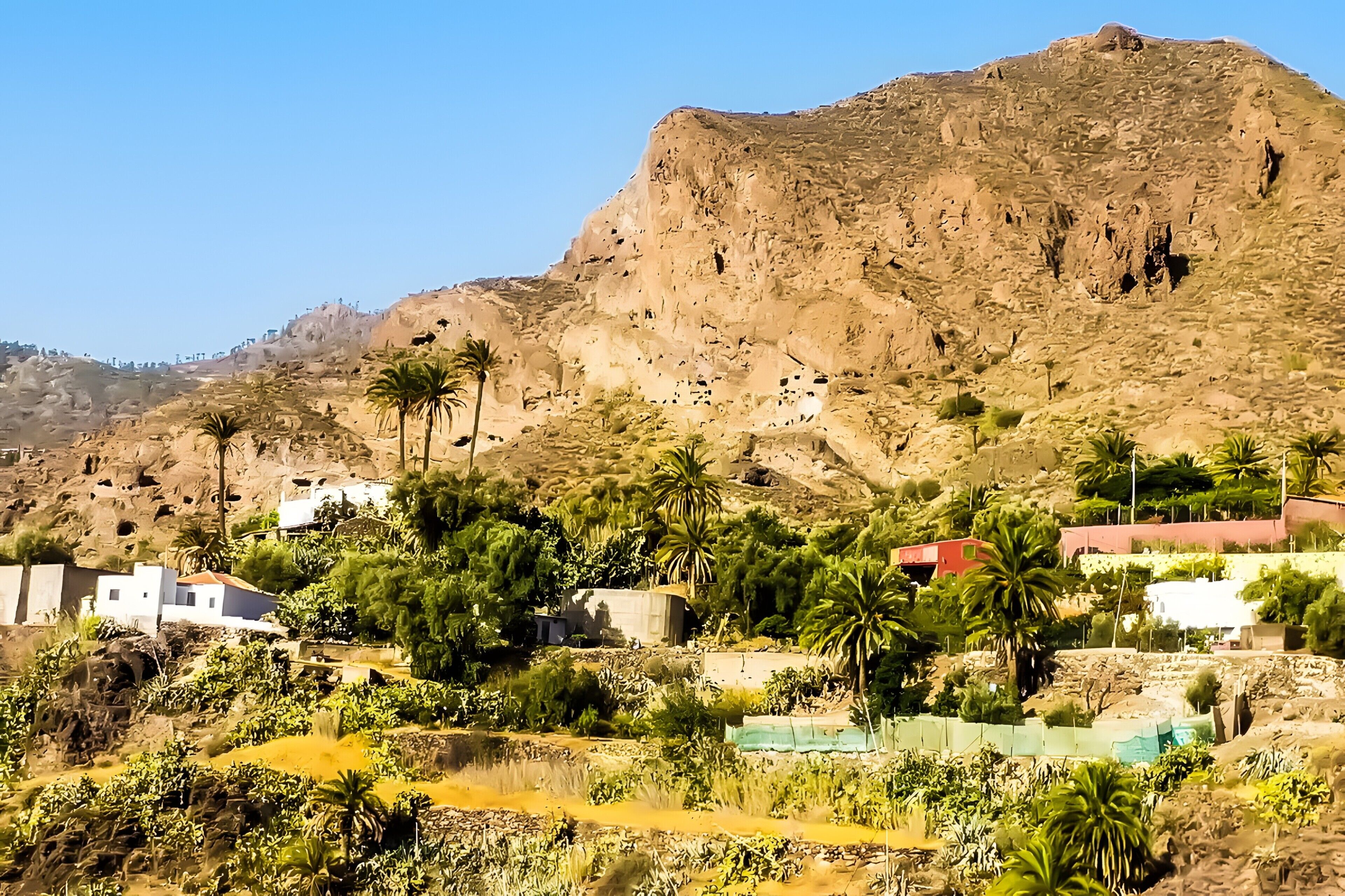 A mountainous landscape with buildings, palm trees, and a small water body.