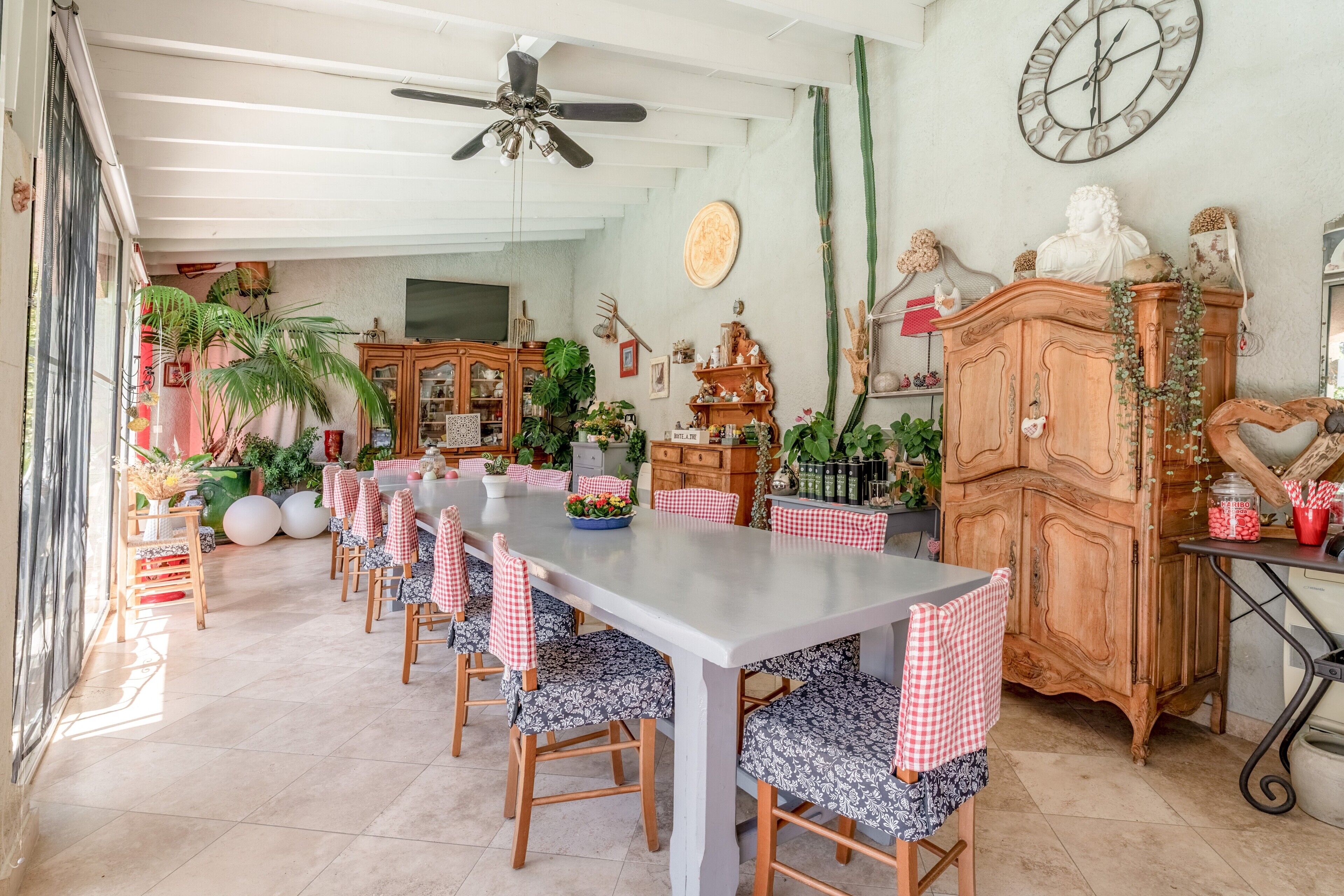 Un coin repas avec une longue table, des chaises à carreaux, un ventilateur de plafond et un cactus accroché au mur.