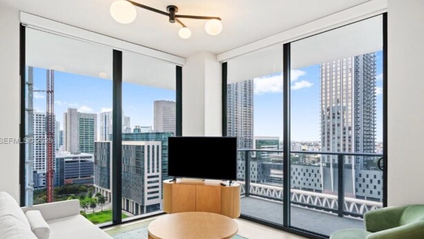A modern living room with a large window, a flat-screen TV, a sofa, a round coffee table, and a green armchair. - Miami World Center 2 BR heart of downtown (Miami)
