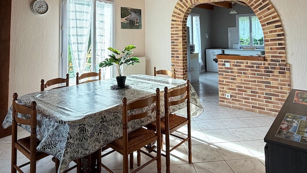 A dining area with a wooden table and chairs, a potted plant, and a brick fireplace.