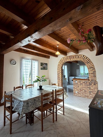 A dining area with a wooden table and chairs, a potted plant, and a brick archway leading to a kitchen.. Country House 20 Minutes from Salers with Private Terrace and Garden