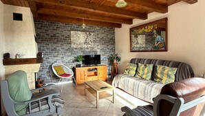 A cozy living room with a stone fireplace, wooden ceiling beams, a sofa, a coffee table, and a television.