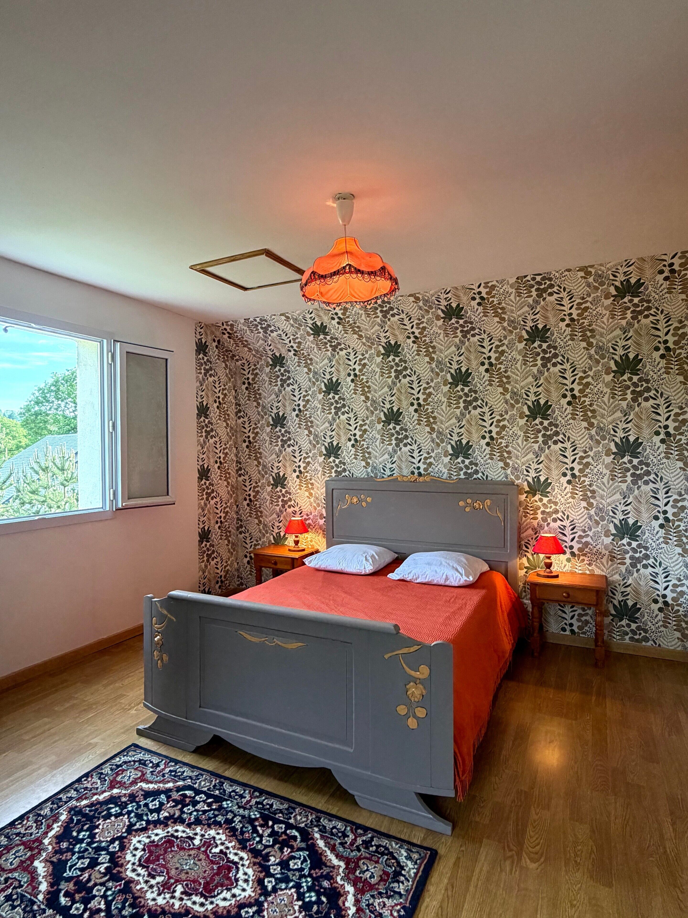 Une chambre à coucher avec un lit, un papier peint à motifs, une fenêtre et un tapis.