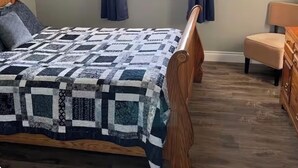 A bedroom with a wooden bed, a window with curtains, a chair, and a dresser. - Cozy Cottage in Gros Morne - Cow Head, NL 
Sunset Lodging - Pet Friendly! (Cow Head)