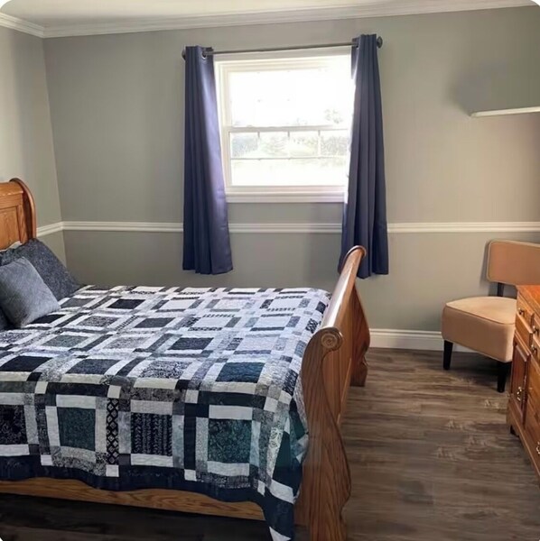 Une chambre à coucher avec un lit en bois, une fenêtre avec des rideaux, une chaise et une commode.