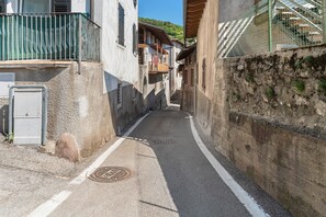 A narrow street with buildings on either side, a manhole cover on the road, and a green fence on the left. - Casa Sole Trento, Trentino Alto Adige (Romagnano)