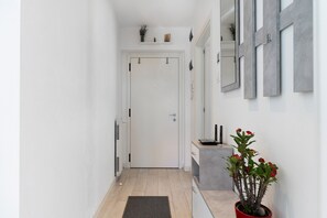 A narrow hallway with a white door, a radiator, a small potted plant with red flowers, and a grey cabinet. - Casa Sole Trento, Trentino Alto Adige (Romagnano)