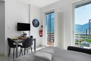 Een moderne hotelkamer met een bed, een bureau met een flatscreen televisie, een zithoek en een balkon met uitzicht op de bergen.