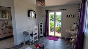 A room with a desk, chair, and a view of a garden through a sliding door. - Romantic 35 m² Guest Room with Mountain View, Wi-Fi, and Air Conditioning (Égliseneuve-près-Billom)