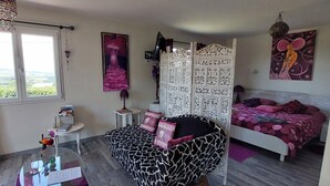 A bedroom with a bed, a chair, a table, a window, and a decorative partition. - Romantic 35 m² Guest Room with Mountain View, Wi-Fi, and Air Conditioning (Égliseneuve-près-Billom)