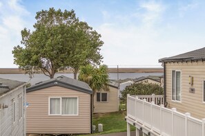 A row of mobile homes with a large tree in the foreground. - Cabin Sleeps 8 - Pools, Parking, Pets (Weymouth)