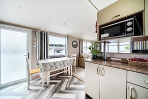 A modern kitchen with a dining area, large windows, and a herringbone floor pattern. - Cabin Sleeps 8 - Pools, Parking, Pets (Weymouth)