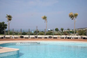 Una piscina con lettini, palme e vista sull'oceano.