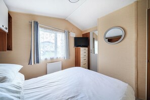 A bedroom with a bed, a television, a mirror, and a window with curtains. - Cabin Sleeps 8 - Pools, Parking, Pets (Weymouth)