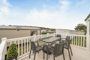 A deck with a table and chairs, surrounded by a white railing, overlooking a residential area with mobile homes. - Cabin Sleeps 8 - Pools, Parking, Pets (Weymouth)