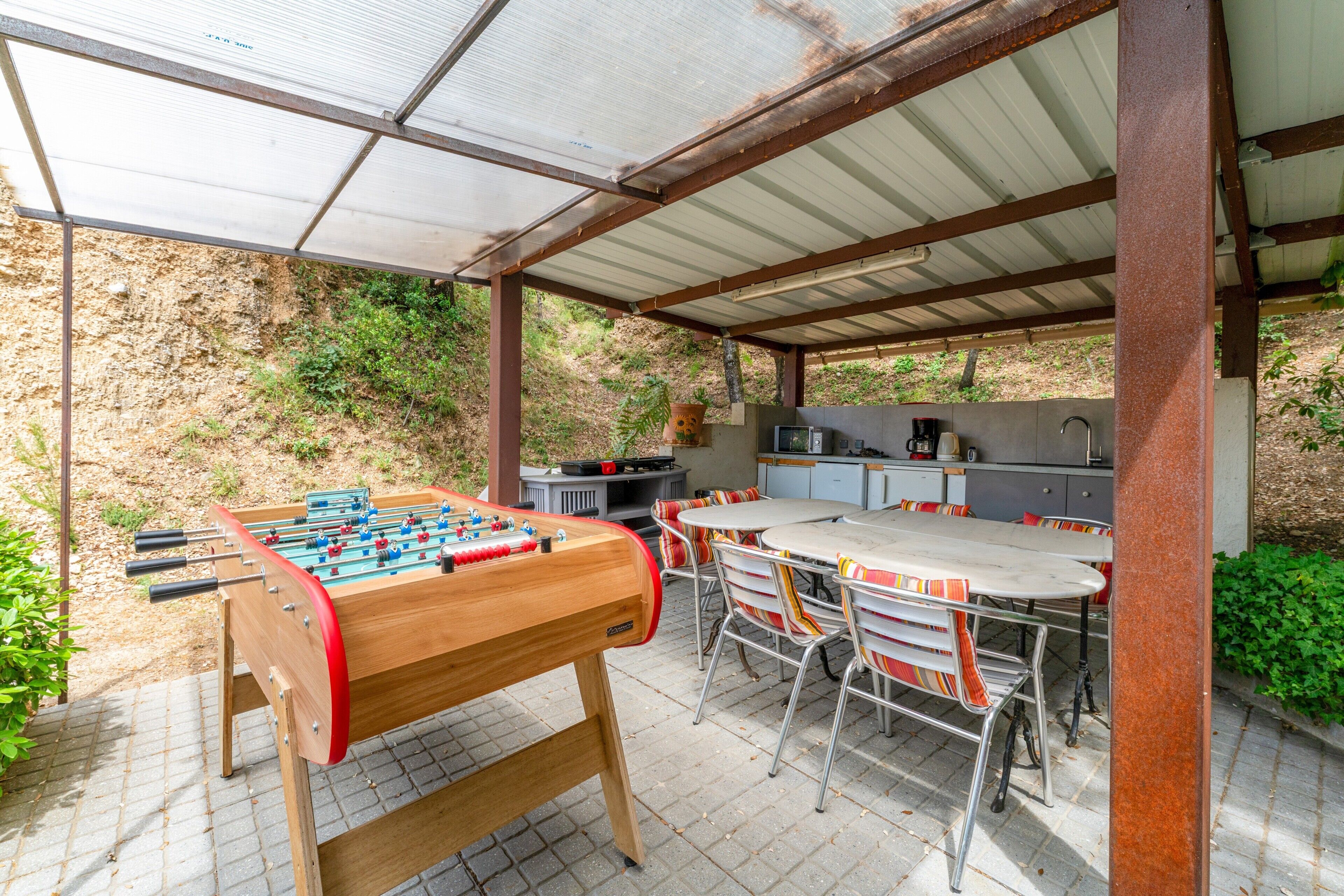 Um pátio externo com mesa de futebol de mesa, churrasqueira e área de refeições com cadeiras e mesa.
