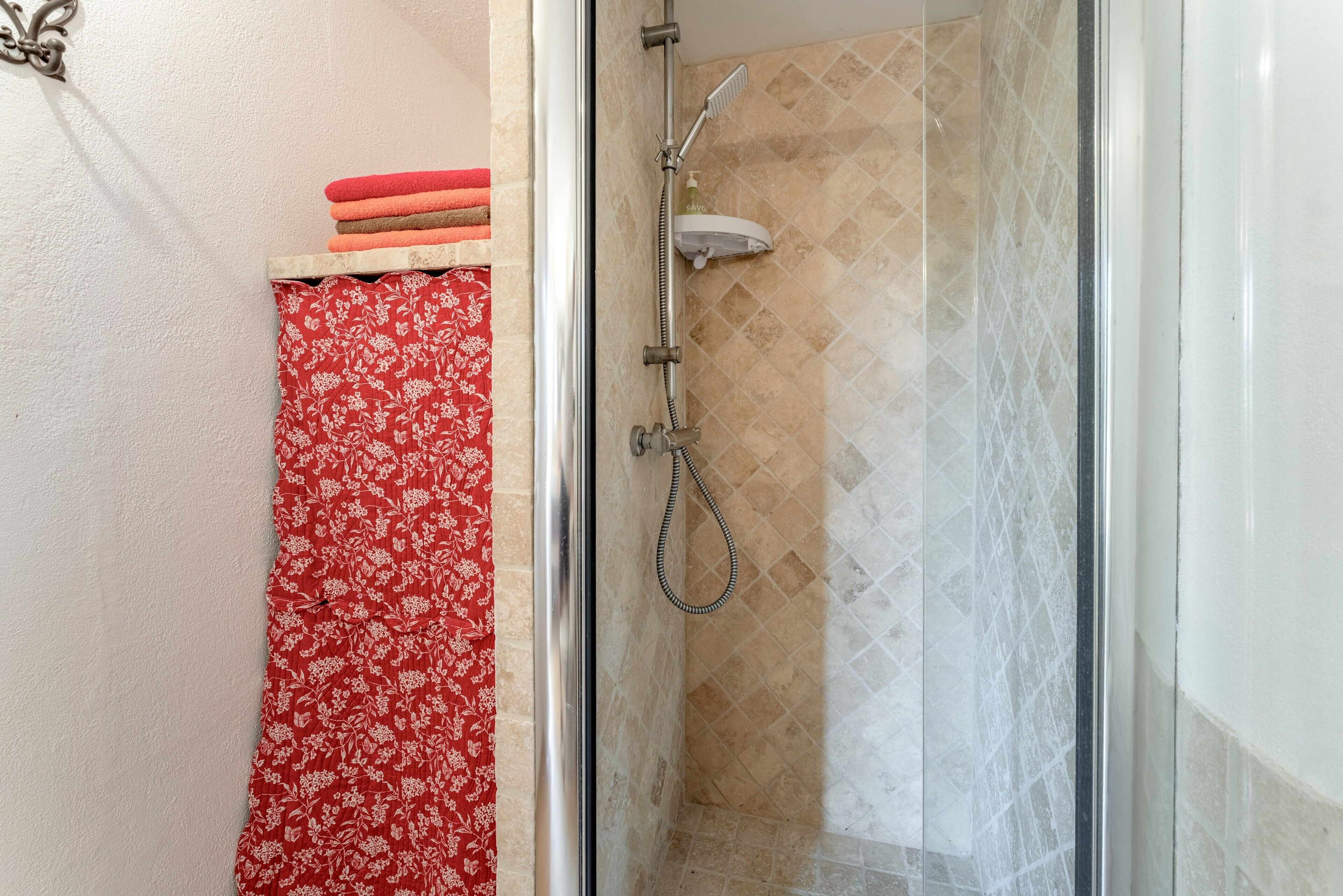 Un espace douche doté d’une porte en verre, d’un mur carrelé et d’un rideau à motifs floraux rouges.