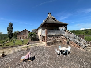 A stone house with a balcony, a staircase, and outdoor seating. - Gîte L'Oustal – Domaine Les Planes with Shared Pool, Private Terrace, and Wi-Fi (Nauviale)