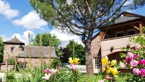 A stone building with a thatched roof, surrounded by a garden with various flowers and a large tree. - Guest Room “Beaucaire” with Shared Pool, Garden, and Wi-Fi (Nauviale)