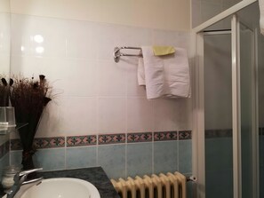 Une salle de bain comprenant un lavabo, un porte-serviettes avec deux serviettes, un radiateur et un espace douche.