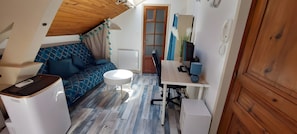 A compact room with a sofa, a small round table, a desk with a computer, and a wooden ceiling.