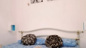 Una cama con cubierta roja, dos almohadas estampadas y una colcha azul con motivos florales.