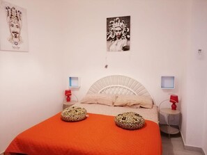 Une chambre à coucher avec un lit, deux oreillers, une couverture rouge, deux tables de chevet avec des lampes et deux tableaux accrochés au mur.
