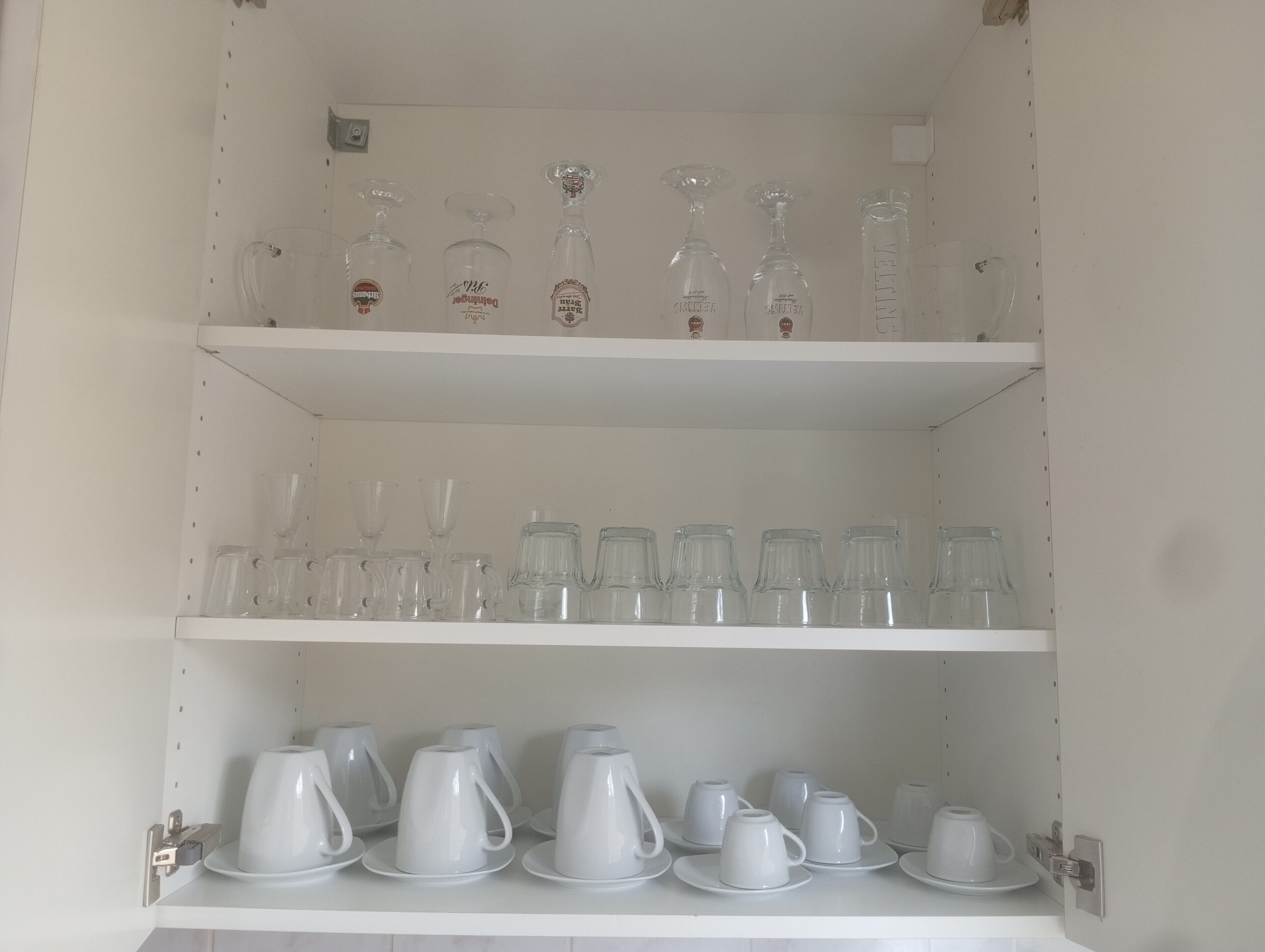 A white shelving unit with clear glassware and white ceramic cups.