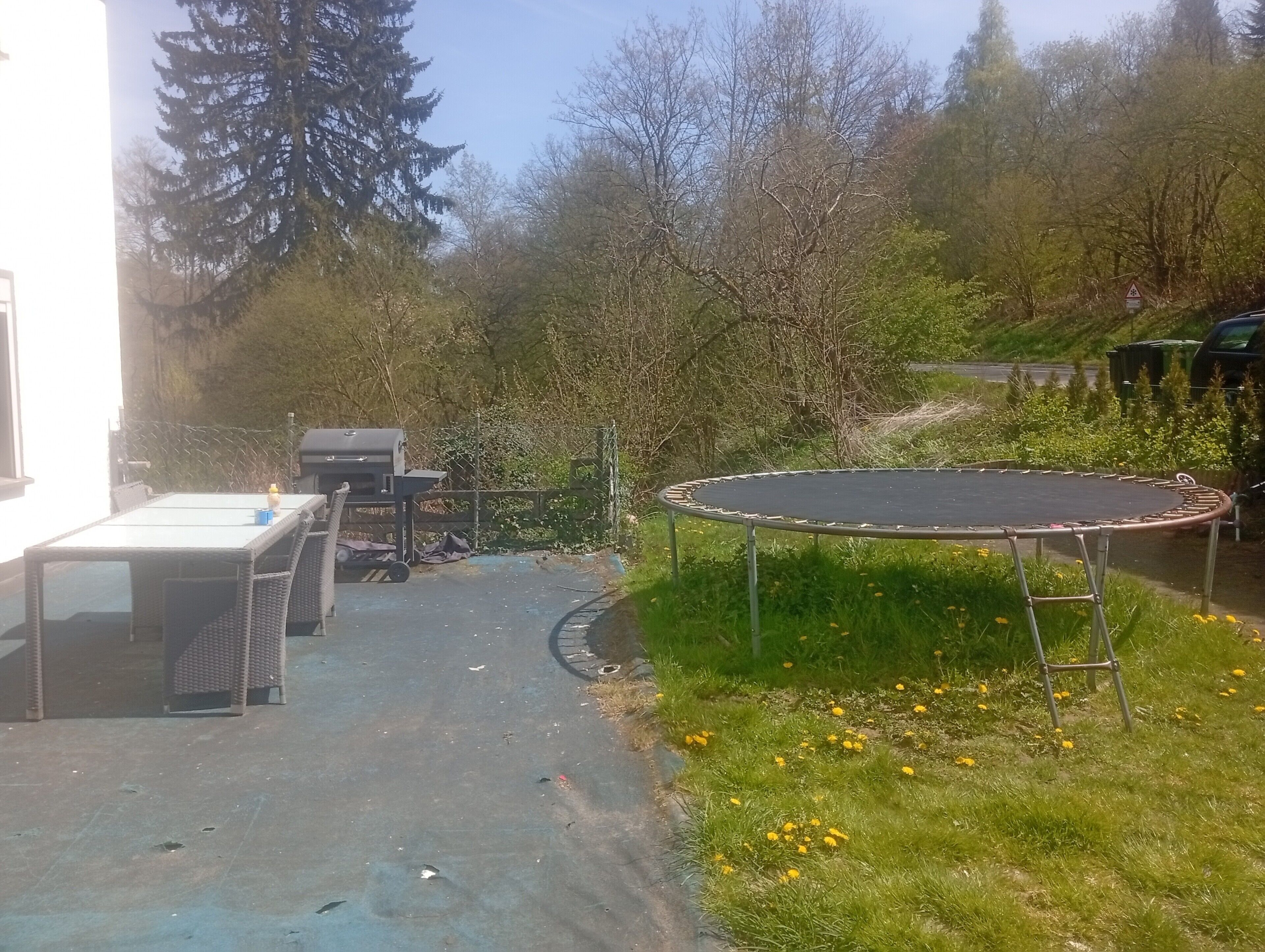 Een achtertuin met een trampoline, een tafel en stoelen.