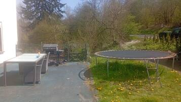 Een achtertuin met een trampoline, een tafel en stoelen.