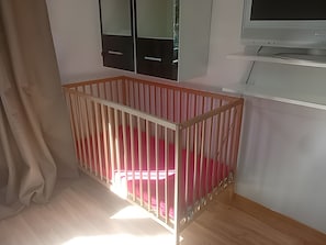 Une chambre avec un berceau en bois, une télévision et une armoire.