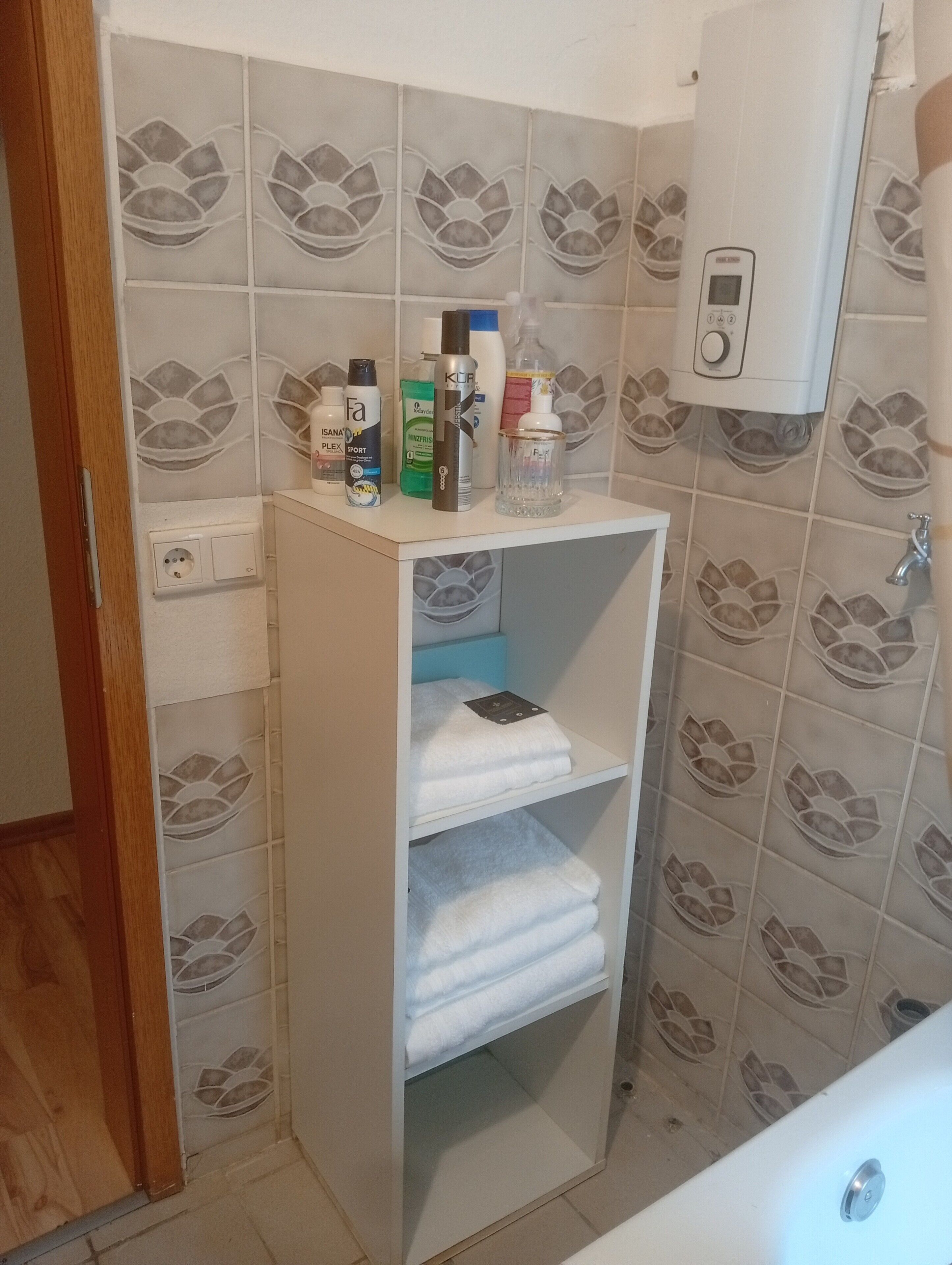 A bathroom with a towel shelf, toiletries, and a water heater.