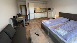 A compact hotel room with a bed, a small desk, a couch, and a kitchenette. - Studio Apartment 'Luv Lee Duhnen 02' with Private Terrace, Shared Garden and Wi-Fi (Cuxhaven)