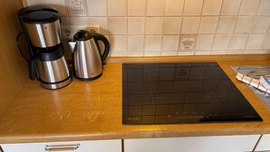 A kitchen with a coffee maker, kettle, induction cooktop, and a tiled backsplash. - Studio Apartment 'Luv Lee Duhnen 02' with Private Terrace, Shared Garden and Wi-Fi (Cuxhaven)