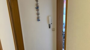 A hallway with a wooden door on the left, a wall-mounted telephone, and a decorative fish wall hanging. - Studio Apartment 'Luv Lee Duhnen 02' with Private Terrace, Shared Garden and Wi-Fi (Cuxhaven)