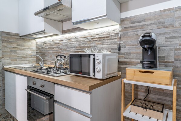 A modern kitchen with a microwave, toaster, kettle, and coffee maker on a wooden countertop.