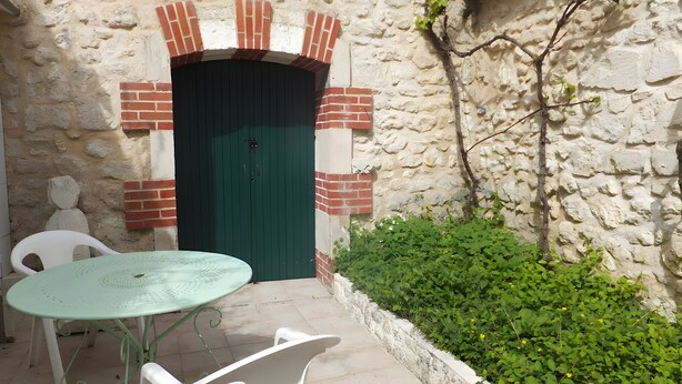 Un muro de piedra con una puerta verde, una silla de plástico blanco y una pequeña mesa.