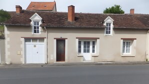 Un edificio de dos pisos con fachada blanca, puerta de garaje y dos ventanas con contraventanas.