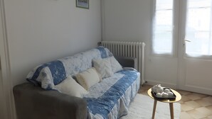 Una sala de estar con un sofá, un radiador, una pequeña mesa con objetos y dos cuadros en la pared.