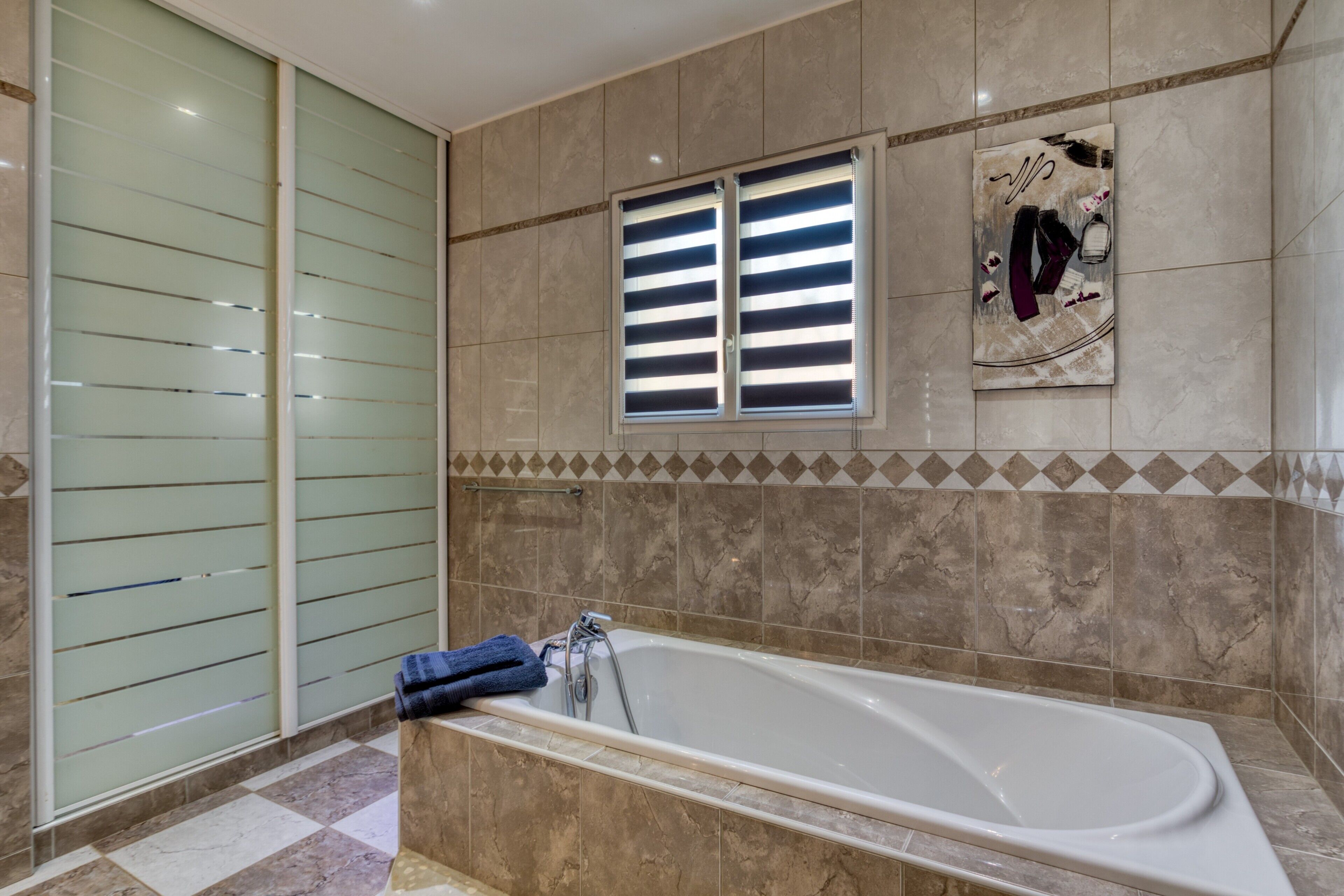 A modern bathroom with a large bathtub, a glass shower enclosure, and a decorative wall piece.