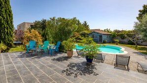 Patio con piscina, sillas azules y plantas en macetas.