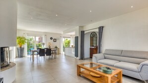Un amplio salón con sofá, una mesa de centro de cristal, zona de comedor con sillas y una cocina al fondo.