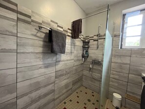A modern bathroom with a shower, tiled walls, a glass door, and a window.